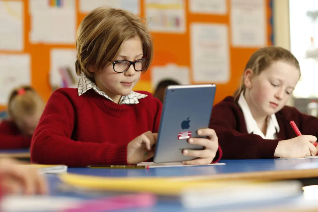 Primary school students learning with tablets and pencils in a classroom.