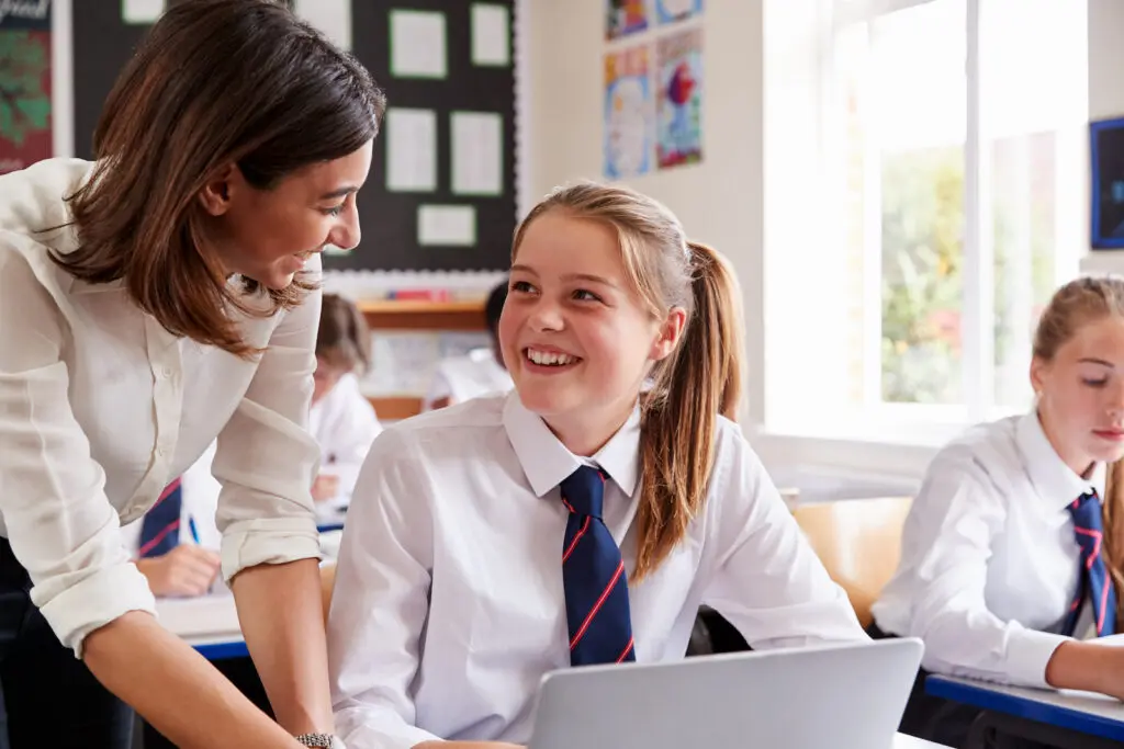 Teacher helping a student with a laptop in a classroom.