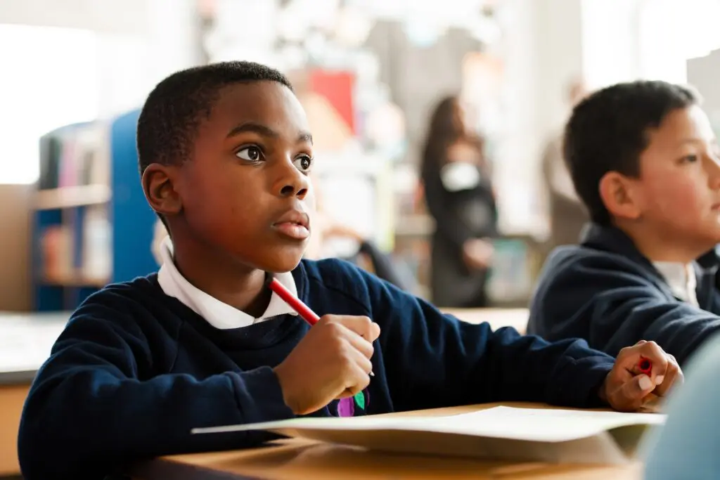 Boy in school uniform holding a pencil, looking thoughtful in class.