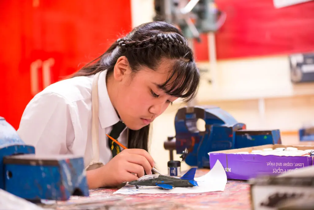 Teenage girl in school uniform carefully painting a model airplane.