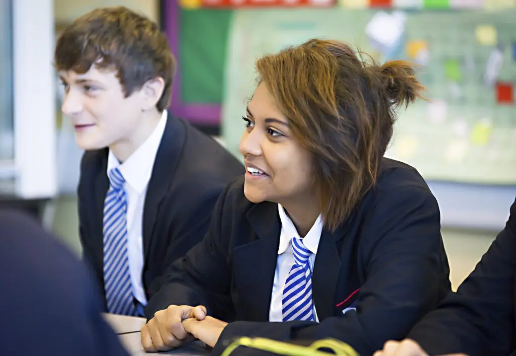 Students in school uniforms listen attentively in a classroom.