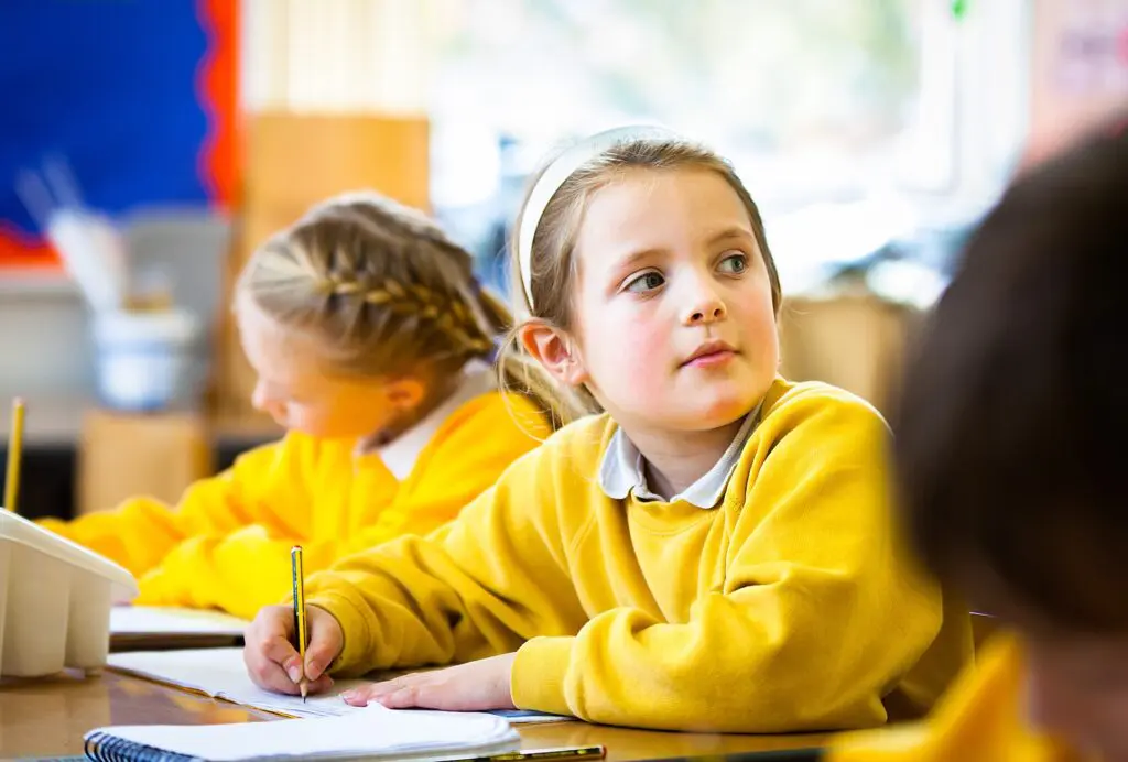 Primary student in yellow uniform writing in class.