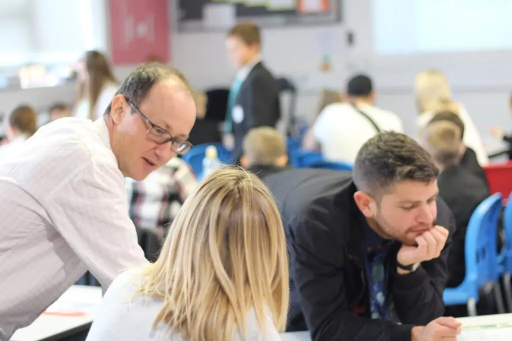 A classroom scene with two teachers helping students with their work.