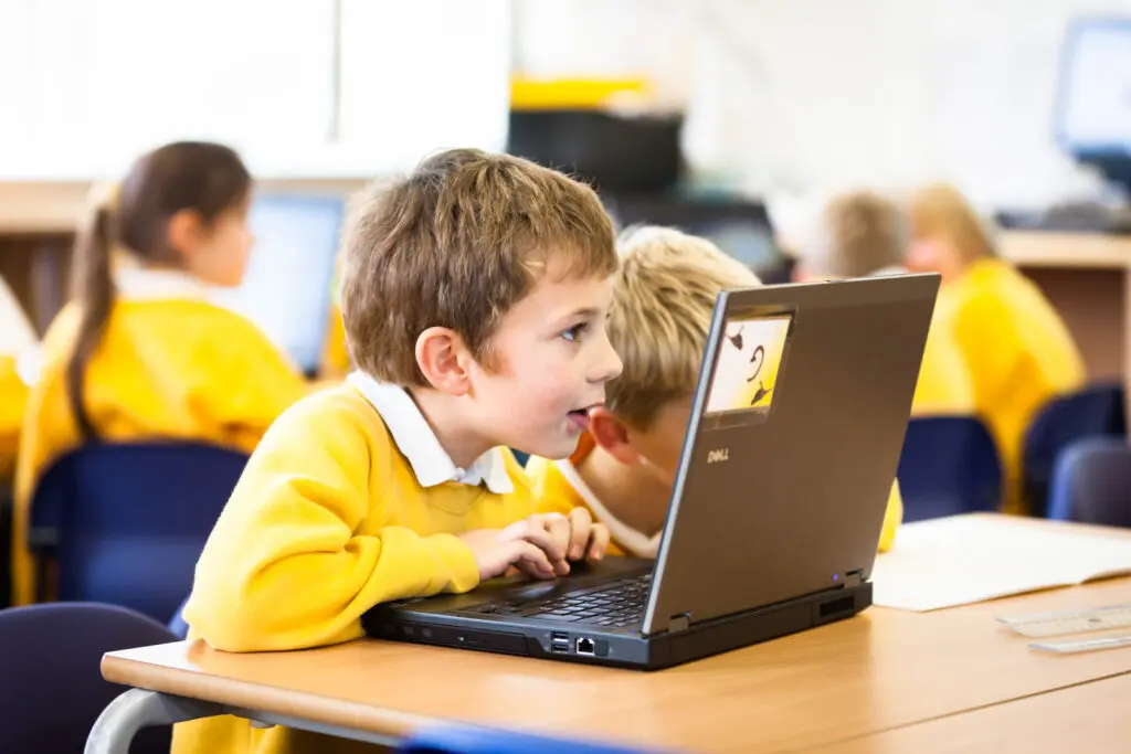 Primary school children in yellow uniforms using laptops in a classroom.