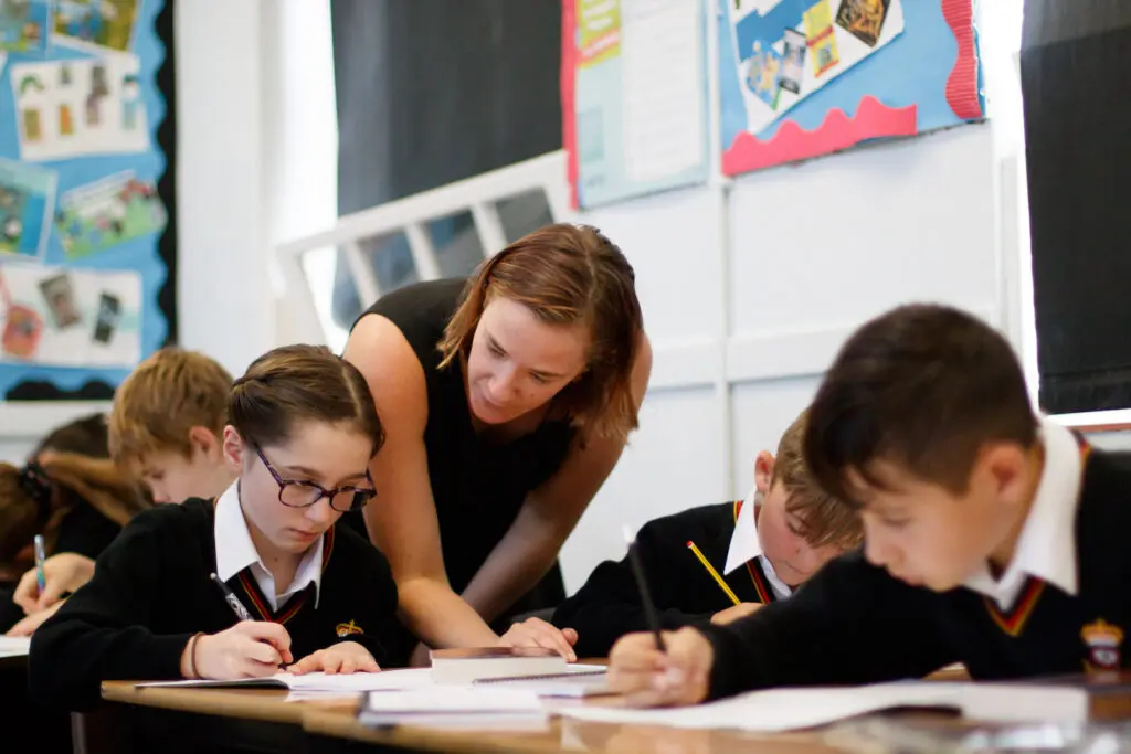 A teacher assisting students working at their desks in a classroom.