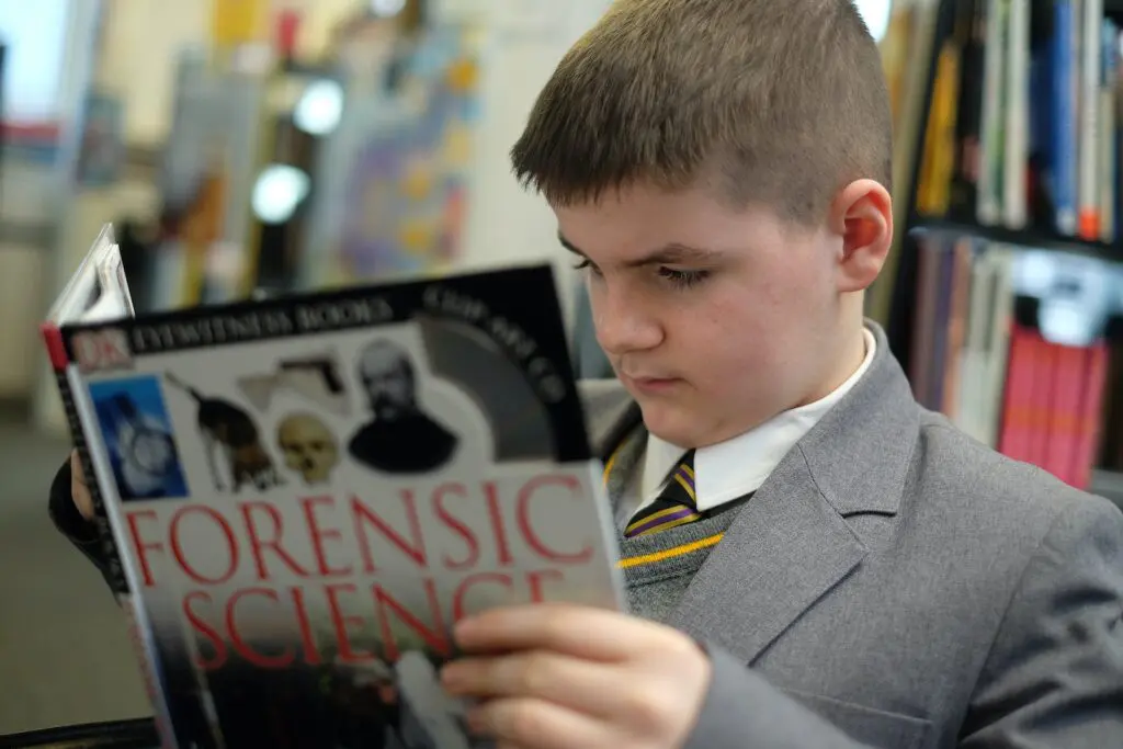 A student in a school uniform reading a book in a library.