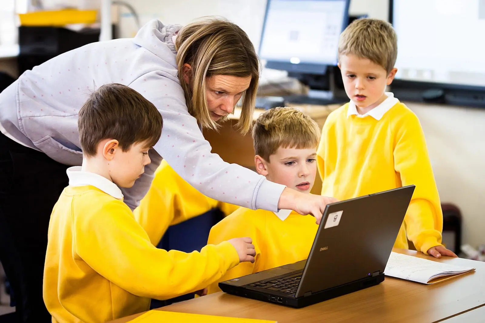 Teacher helping three students using a laptop
